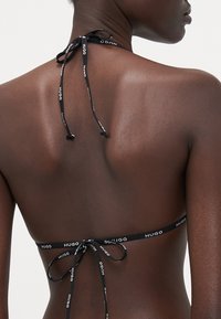 Top bikini nero con lacci regolabili. Presenta spalline decorate con il logo e un design minimalista. Texture liscia e silhouette semplice.