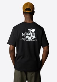 Černé bavlněné tričko s bílým grafickým textem "THE NORTH FACE" a ilustrací hor na zádech. Krátké rukávy a volný střih.