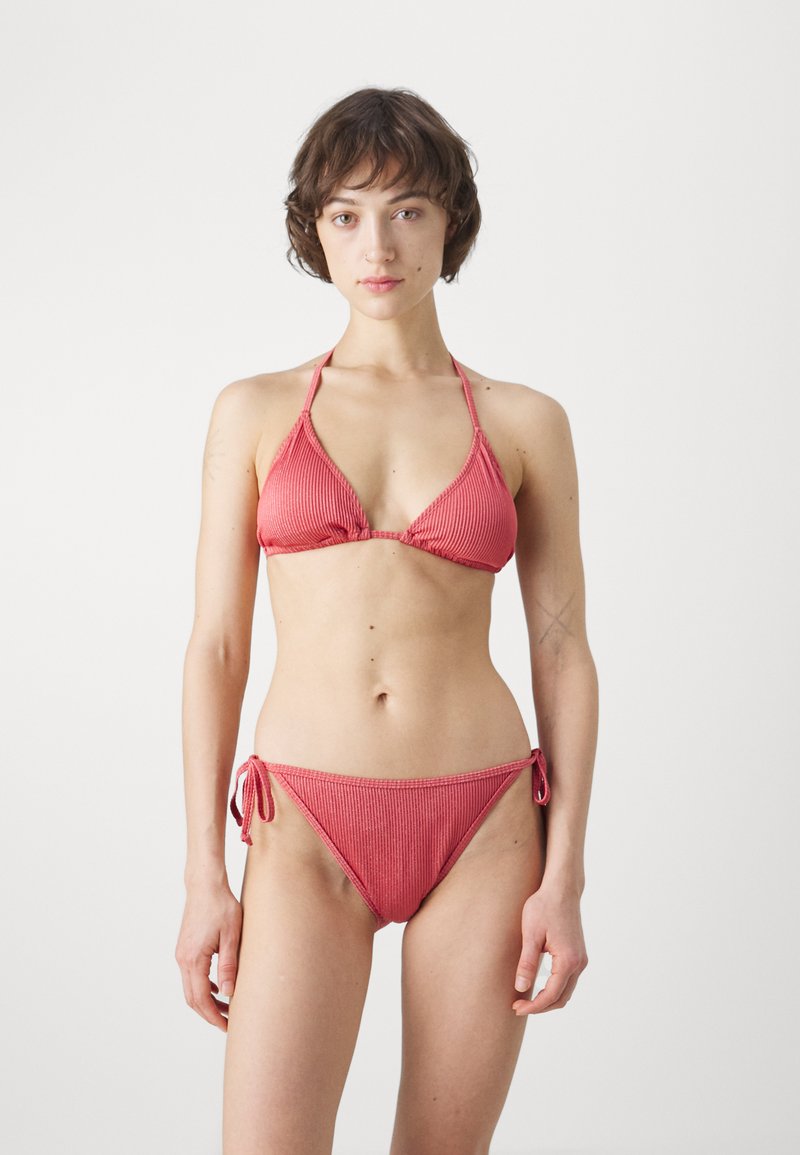 Crveni rebrasti bikini s trokutastim gornjim dijelom s podesivim trakama i donjim dijelom s niskim strukom i vezicama sa strane. Glatka tekstura i minimalni dodaci.