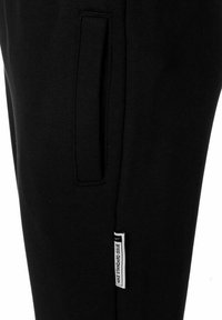 Zwarte joggingsbroek met een taps toelopend ontwerp, zijzak en een label van stof met "NIKE STANDARD ISSUE" op de zoom genaaid.