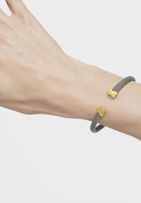 Pulsera de malla gris con dos acentos en forma de oso en tono dorado, con un diseño flexible que se adapta a la muñeca.