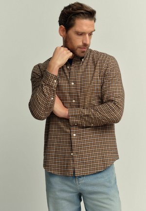 Bruine geruite shirt gemaakt van lichtgewicht stof, met een knoopsluiting aan de voorkant en opgerolde mouwen, gecombineerd met lichtblauwe jeans.