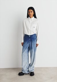 Λευκό πουκάμισο με μακριά μανίκια και τσέπη στο στήθος, συνδυασμένο με ανοιχτό μπλε φαρδιά τζιν παντελόνια και μαύρες χοντρές πατούσες.