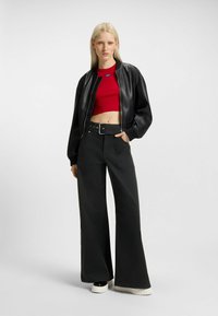 Black leather bomber jacket worn over a red cropped top, paired with high-waisted black wide-leg pants and chunky white platform shoes.