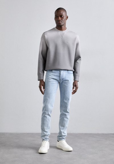 Felpa grigia in cotone con colletto a costine; jeans slim-fit blu chiaro; sneaker bianche; design semplice, senza loghi o modelli visibili.