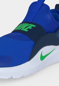 Μπλε sneaker τύπου slip-on της Nike με πράσινο λογότυπο σε μαύρο λουράκι και λευκή σόλα με πράσινο σήμα Nike στην πλευρά.