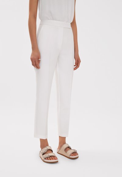 Pantalones blancos ajustados con un corte slim, que cuentan con una cintura estructurada y dos bolsillos laterales, combinados con sandalias de plataforma color tostado.