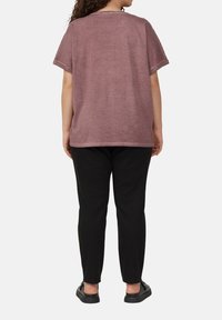 Lässiges, kurzärmliges, mauvefarbenes T-Shirt aus Baumwollmischung mit Rundhalsausschnitt, kombiniert mit schwarzen, taillierten Hosen und schwarzen flachen Schuhen.