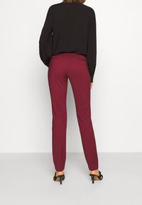 Pantalon bordeaux à coupe ajustée, avec une texture de tissu lisse, des poches arrière et une taille mi-haute, associé à un haut noir.