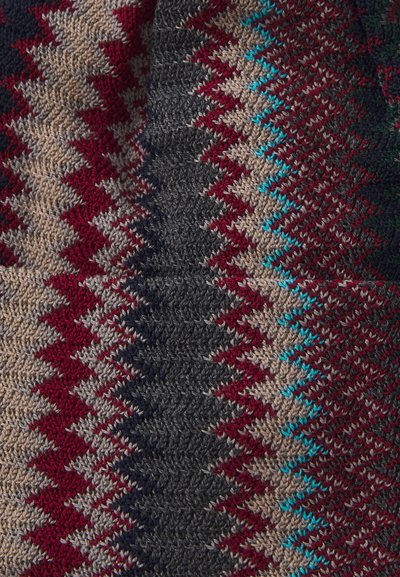 Knitted fabric with zigzag pattern in beige, red, black, and turquoise colors creating a textured geometric design.