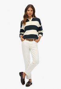 Navy and white striped sweater with a collar, paired with cream pants and burgundy loafers. Braided belt and slightly loose fit.