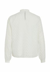 Blouse blanche à manches longues avec un motif texturé en chevrons, des poignets élastiques, un col froncé haut et une fermeture à bouton en forme de clé au dos.