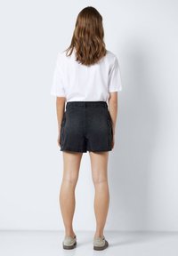 Schwarze Jeansshorts mit hoher Taille, Seitentaschen und einer strukturierten Oberfläche. Kombiniert mit einem schlichten weißen T-Shirt und grauen Schuhen.