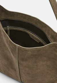 Zielona torba na ramię z zamszu o miękkiej fakturze, z wewnętrzną kieszenią na zamek i kontrastowym czarnym podszewką. Okrągły kształt górnej krawędzi.