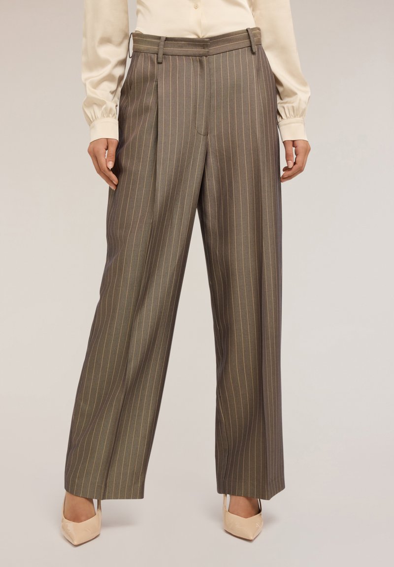 Hnědé kalhoty s jemným proužkem, vysokým pasem, širokými nohavicemi a předními záhyby. Tkanina vypadá hladce s jemným leskem.