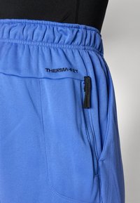 Light blue Therma-FIT pants with an elastic waistband, featuring a side zip pocket and smooth texture. Branding visible on the front.
