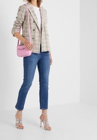 Blazer a cuadros en beige con acentos en verde y rosa, camiseta blanca, jeans ajustados azules y tacones plateados con tiras; bolso cruzado rosa.