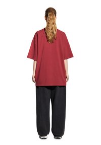 Przesadnie duża bordowa bawełniana koszulka z krótkimi rękawami, połączona z luźnymi ciemnoniebieskimi spodniami dżinsowymi. Materiał ma gładką teksturę i subtelne detale w szwach.