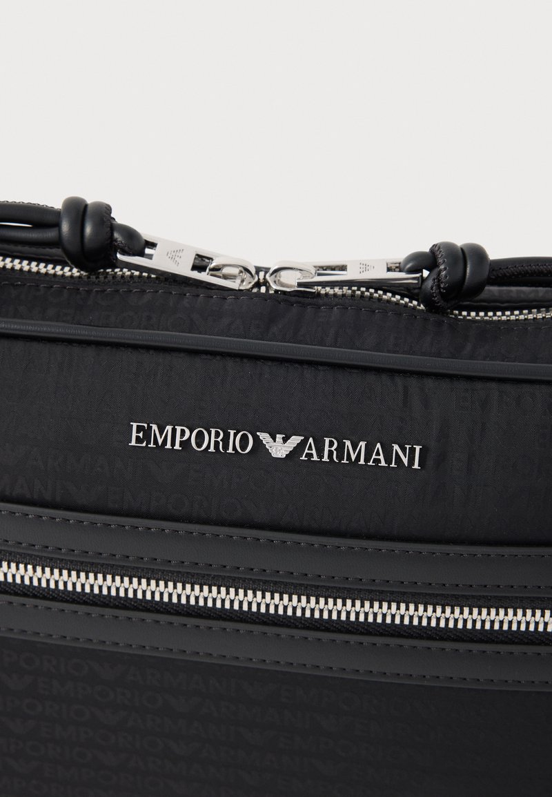 Schwarze Nylon-Tasche mit Emporio Armani Logo, silbernen Beschlägen und Reißverschluss mit kontrastierender Naht. Strukturierte Oberflächenmuster sind sichtbar.