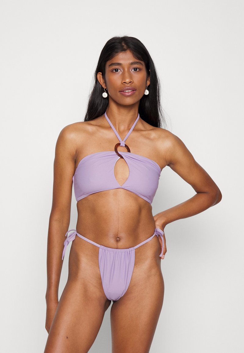Conjunto de biquíni roxo com um top bandeau com um accent circular e uma parte de baixo com laço lateral; textura suave e design de cobertura mínima.