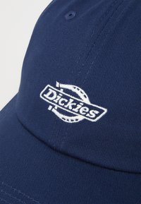 Navy blå baseball caps i bomull med strukturert krone og forhåndsbuet skjerm, med en hvit brodert logo på forsiden.