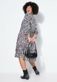 Vestido con estampado de cebra en negro, blanco y rosa, con mangas de tres cuartos. Combinado con un bolso negro y botines negros con tachuelas.