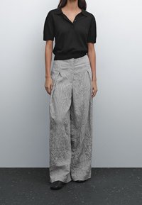 Musta lyhythihainen polo-paita kauluksella, yhdistettynä leveälahkeisiin, tekstuurillisiin musta-valkoisiin raidallisiin housuihin, joissa on etutaskut.