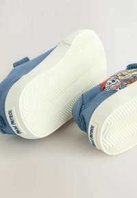 Niebieskie płótnowe buty wsuwane z białą gumową podeszwą, z kreskówkowym wzorem z boku i teksturowanym wzorem grip na spodzie.