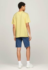 Camiseta de algodón amarilla de manga corta, combinada con pantalones cortos de mezclilla azules. Modelo con zapatillas blancas y calcetines blancos hasta el tobillo.