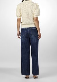 Maglione color crema a maglia con maniche a sbuffo, abbinato a un paio di jeans in denim blu scuro a gamba larga con tasche posteriori e vestibilità rilassata.