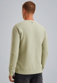 Suéter de color verde claro con textura, con un patrón de punto waffle, mangas largas y puños y dobladillo de canalé. Detalle de logo pequeño en la parte posterior del cuello.