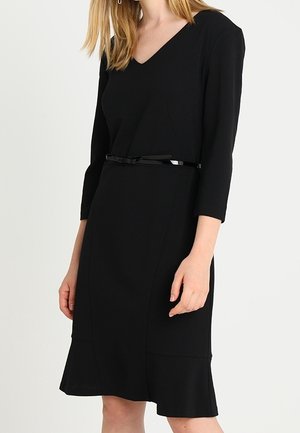 Robe noire à mi-longueur avec des manches trois-quarts, décolleté en V, corsage ajusté, ourlet évasé et une fine ceinture noire à la taille.