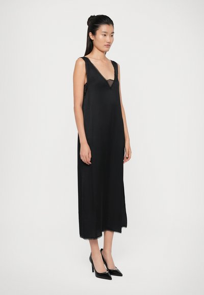 Black sleeveless dress with a v-neck and lace trim. Smooth fabric, flowing silhouette, knee-length, worn with black high heels.