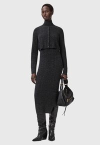 Harmaa ribbineulottu mekko, jossa korkea kaulus, lyhyt napitettava yläosa ja vartalonmyötäinen siluetti, yhdistetty polven korkeisiin mustiin nahkasaappaisiin ja mustaan käsilaukkuun.