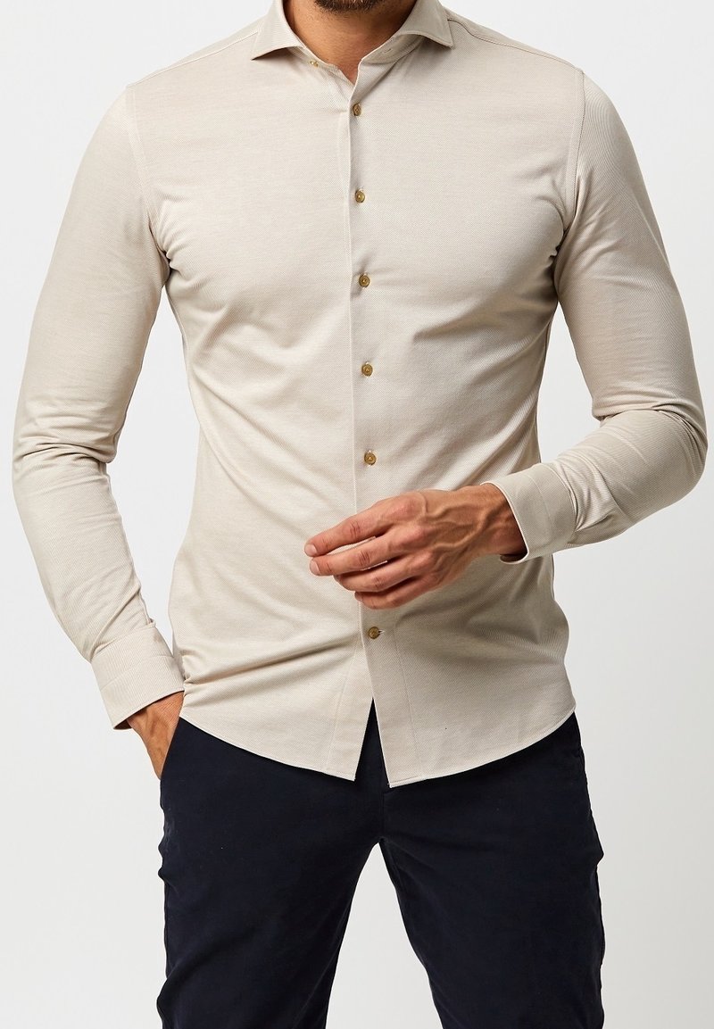 Camicia beige a maniche lunghe con vestibilità slim, tessuto testurizzato e bottoni dorati. Presenta un colletto classico e polsini regolabili.