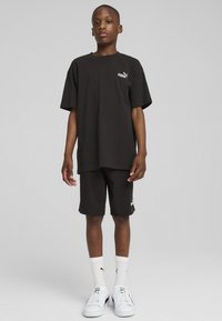 Un ensemble en coton noir composé d'un T-shirt et d'un short, arborant un logo Puma. Le T-shirt a une coupe décontractée, porté avec des baskets blanches et des chaussettes.