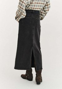 Černá džínová maxi sukně s rozparkem vzadu a dvěma zadními kapsami, v kombinaci s hnědými semišovými kotníkovými botami a vzorovanou károvanou košilí.