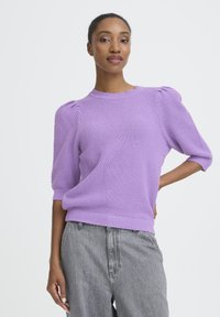 Fliederfarbener Strickpullover mit strukturierter Oberfläche, Puffärmeln sowie geripptem Kragen und Saum. Kombiniert mit grauen Jeans mit weitem Bein.