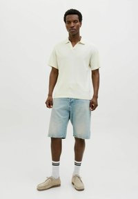 Off-white ribbed anyagú polo póló, világoskék farmer sorttal párosítva. A modellt bézs cipő és fekete csíkos fehér zokni viseli.