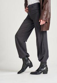 Pantalones gris ajustados con un corte relajado, combinados con botas de tobillo de cuero negro con tachuelas plateadas y puntera en punta.