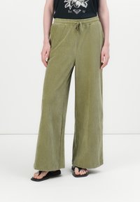 Groene corduroy wijde broek met een textuurfinish, voorzien van een elastische tailleband met een trekkoord. Gecombineerd met een zwart T-shirt en sandalen.