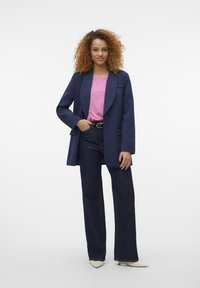Sacou bleumarin, ușor, cu un singur nasture, asortat cu un tricou roz și blugi închiși la culoare cu talie înaltă. Include pantofi bej, cu vârful ascuțit.