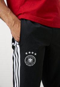 Melni sporta bikses ar baltām svītrām, ar apaļo Vācijas futbola federācijas (Deutscher Fußball-Bund) logotipu un četriem zvaigznēm virs tā. Gluda tekstūra, iekļautas kabatas.