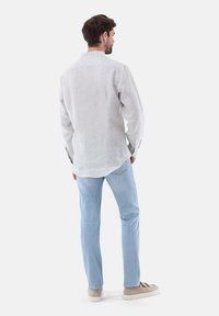 Camicia di lino grigia chiara con colletto, maniche lunghe e polsini con bottone; abbinata a jeans di denim blu chiaro e sneakers beige.