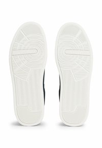 White rubber outsole with textured grip, featuring a circular pattern. Dark navy upper visible at the sides. Stamped logo detail included.