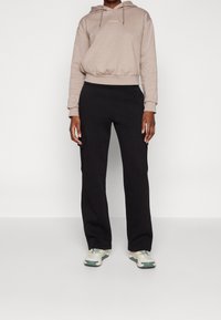 Beige hoodie med dragsko och broderad logga, i kombination med svarta cargobyxor med sidofickor och vita och gröna sneakers.