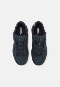 Navy blauwe sneakers met een gladde textuur, voorzien van donkere veters, een versterkte neus en een gevoerde kraag. Logo aanwezig op de tong.