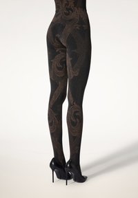 Sorte strømpebukser med udsøgte bronzemønstre og en glimrende tekstur. Sammen med spidse sorte højhælede sko, der fremhæver en tætsiddende silhuet.