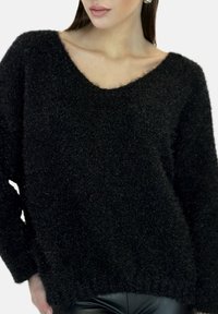 Zwarte, pluizige gebreide trui met een V-hals, lange mouwen en een gestructureerde afwerking, gecombineerd met strakke zwarte broeken.