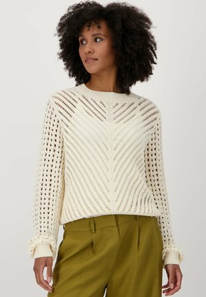 Pull en tricot crème clair avec un motif en chevrons, doté d'un col rond et de poignets côtelés. Associé à un pantalon taille haute vert olive.